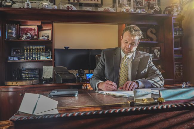 A man in a suit and tie is sitting at a desk writing on a piece of paper.