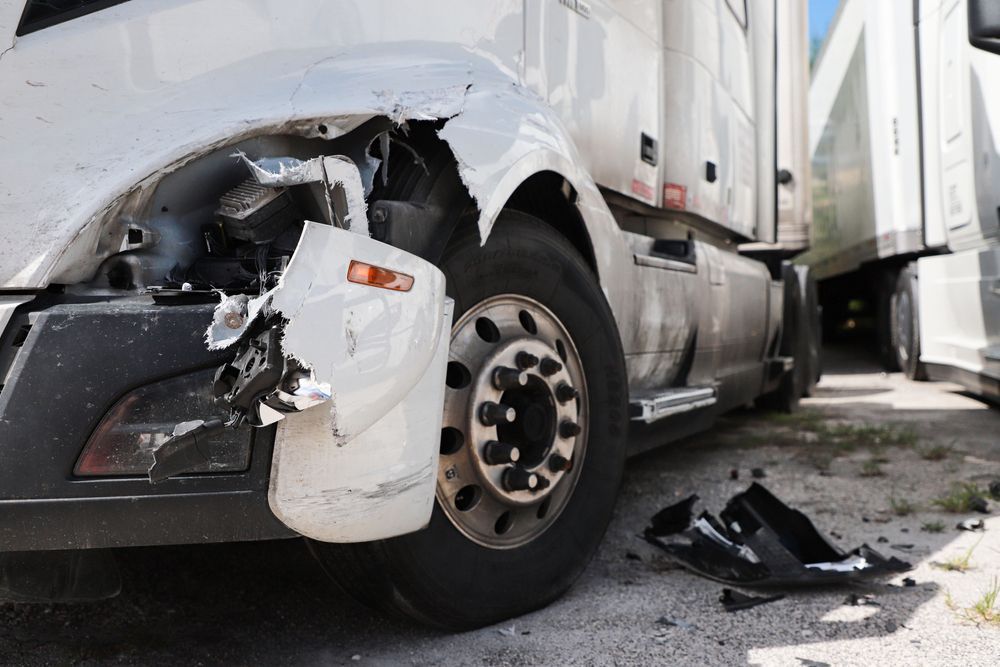 A white semi truck with a damaged front end is parked on the side of the road.