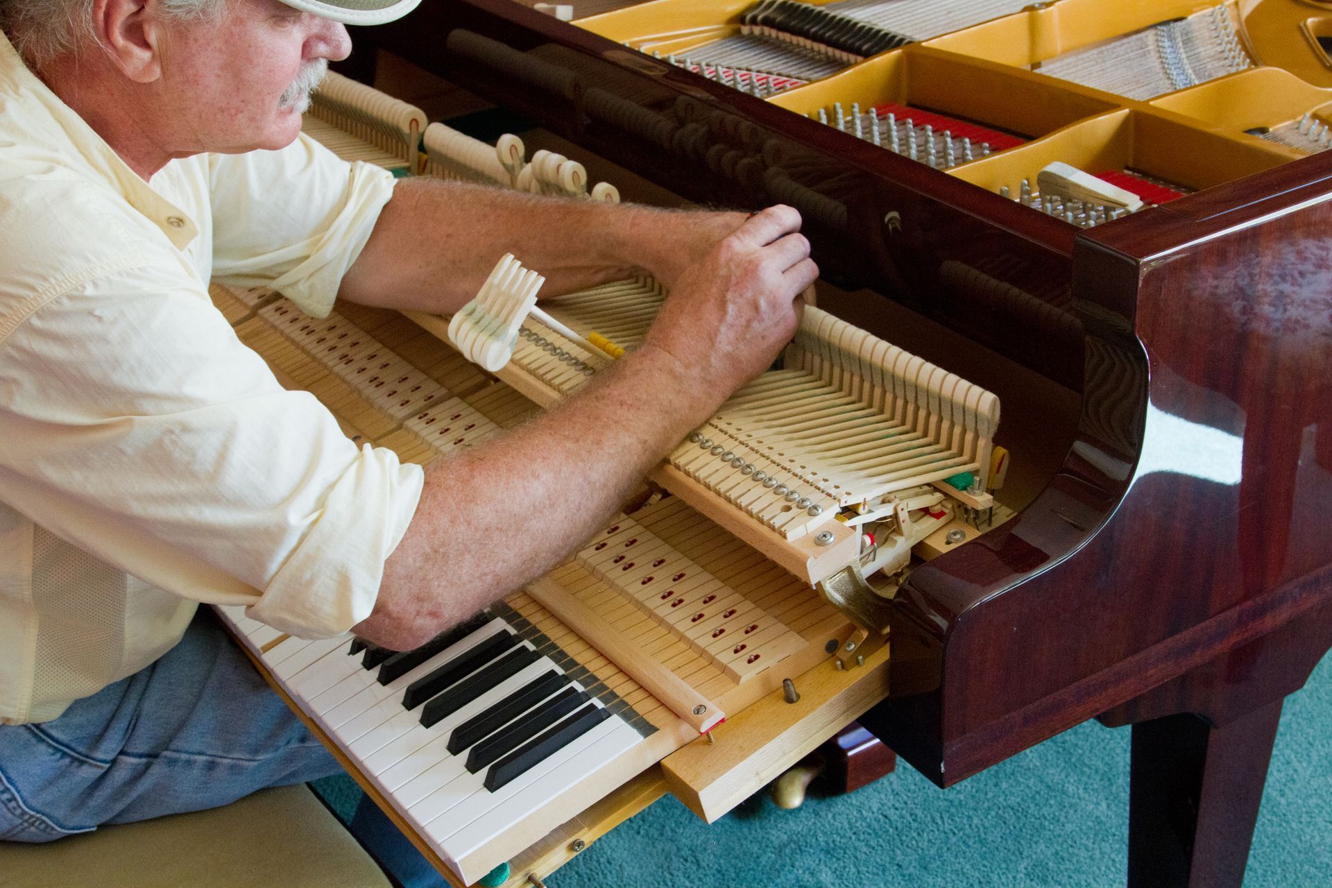 A man is kneeling on the floor working on a piano.