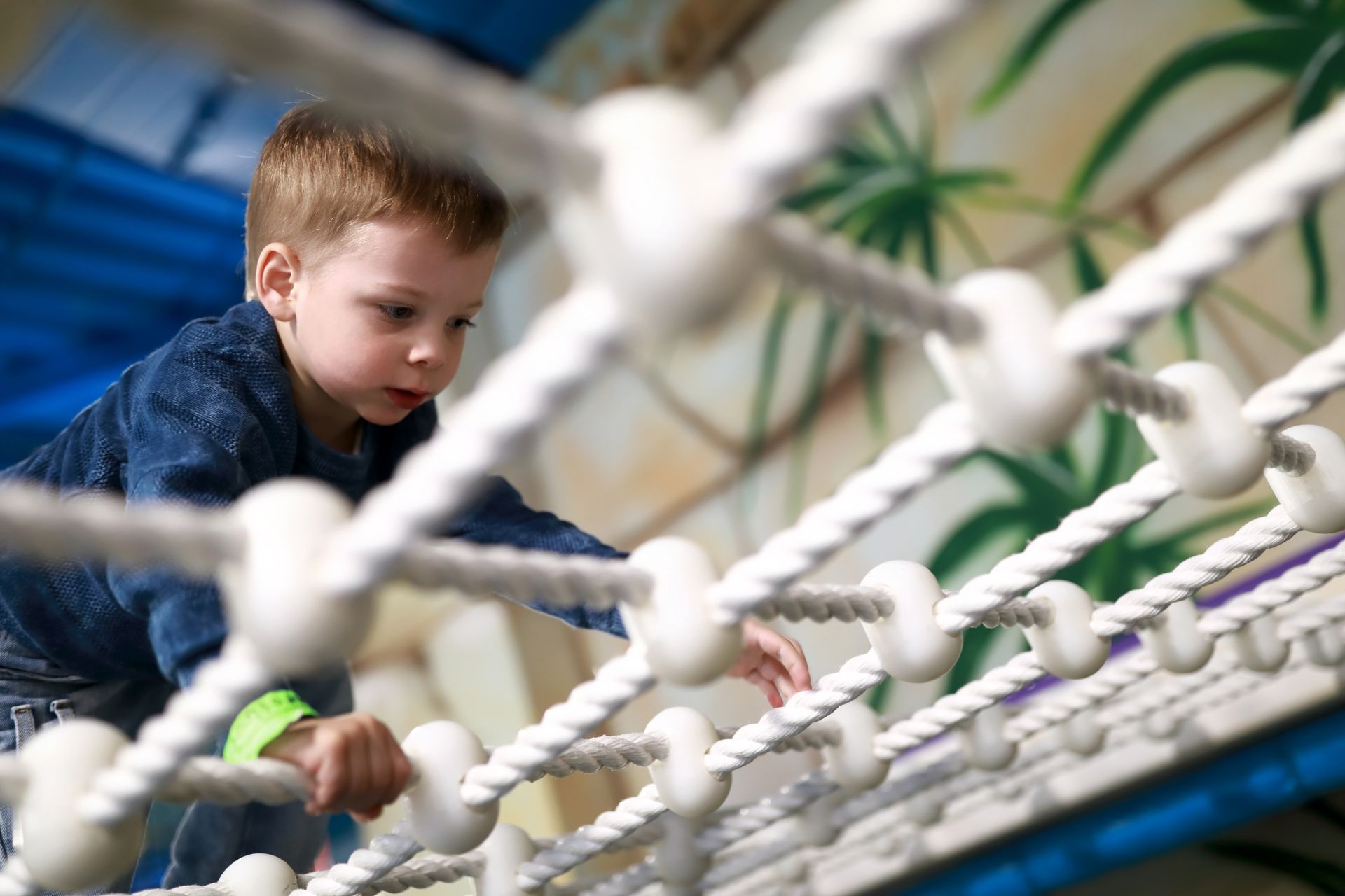 Young boy climbing a rope net in a play area, focused expression.