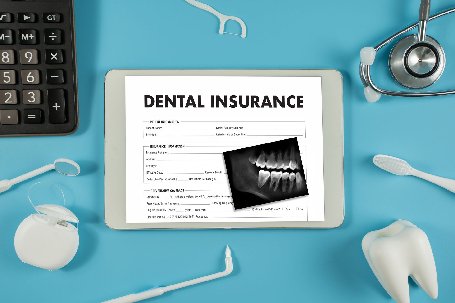 A tablet displaying a dental insurance form and X-ray, surrounded by dental tools and a stethoscope on a blue surface.