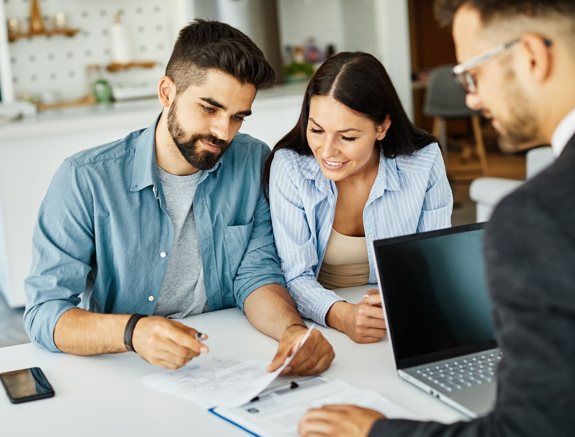 A couple reviewing documents with a financial advisor at a table, looking at a laptop in a well-lit room.