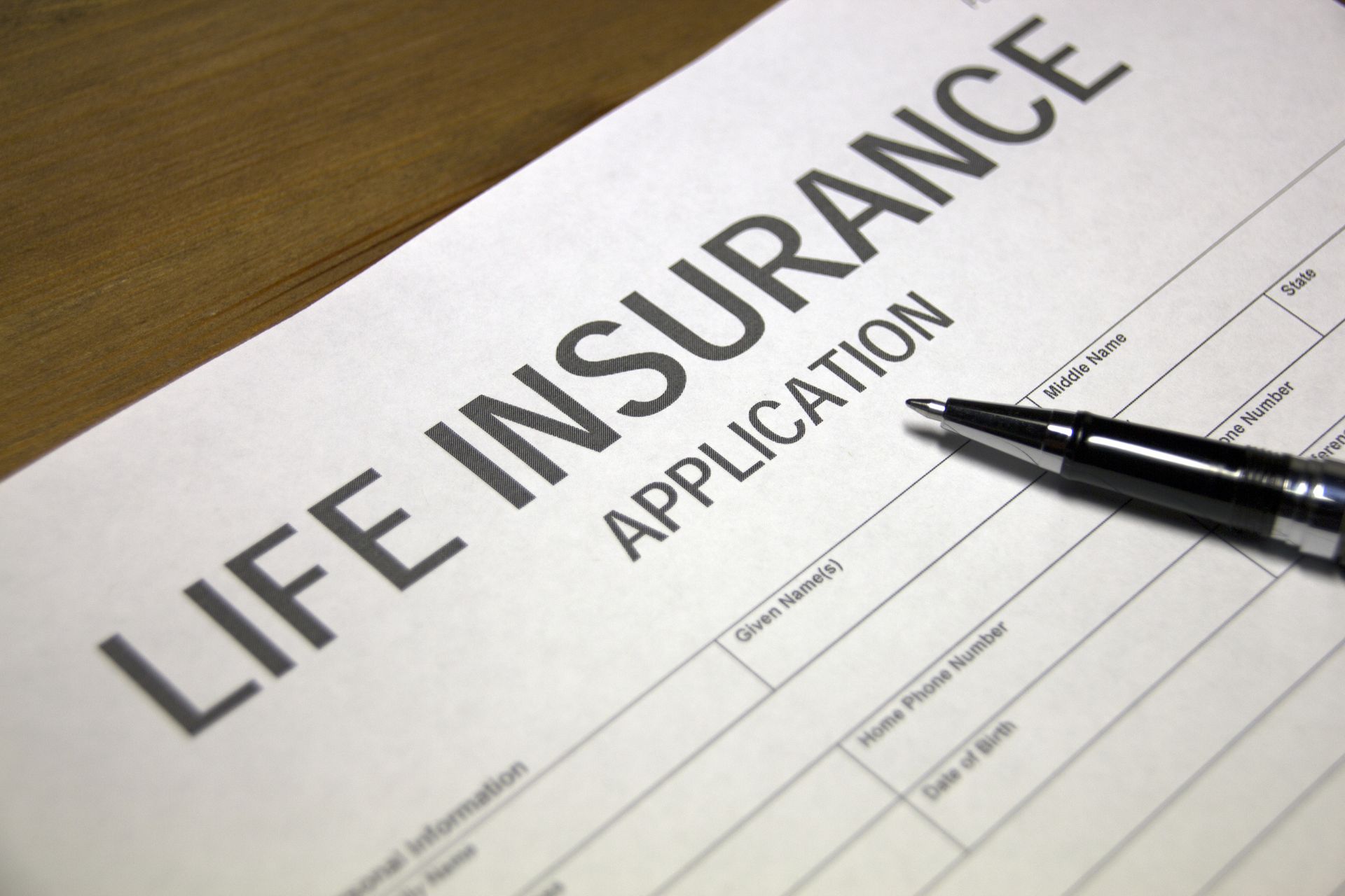 Life insurance application with a pen resting on it. The document is on a wooden surface.