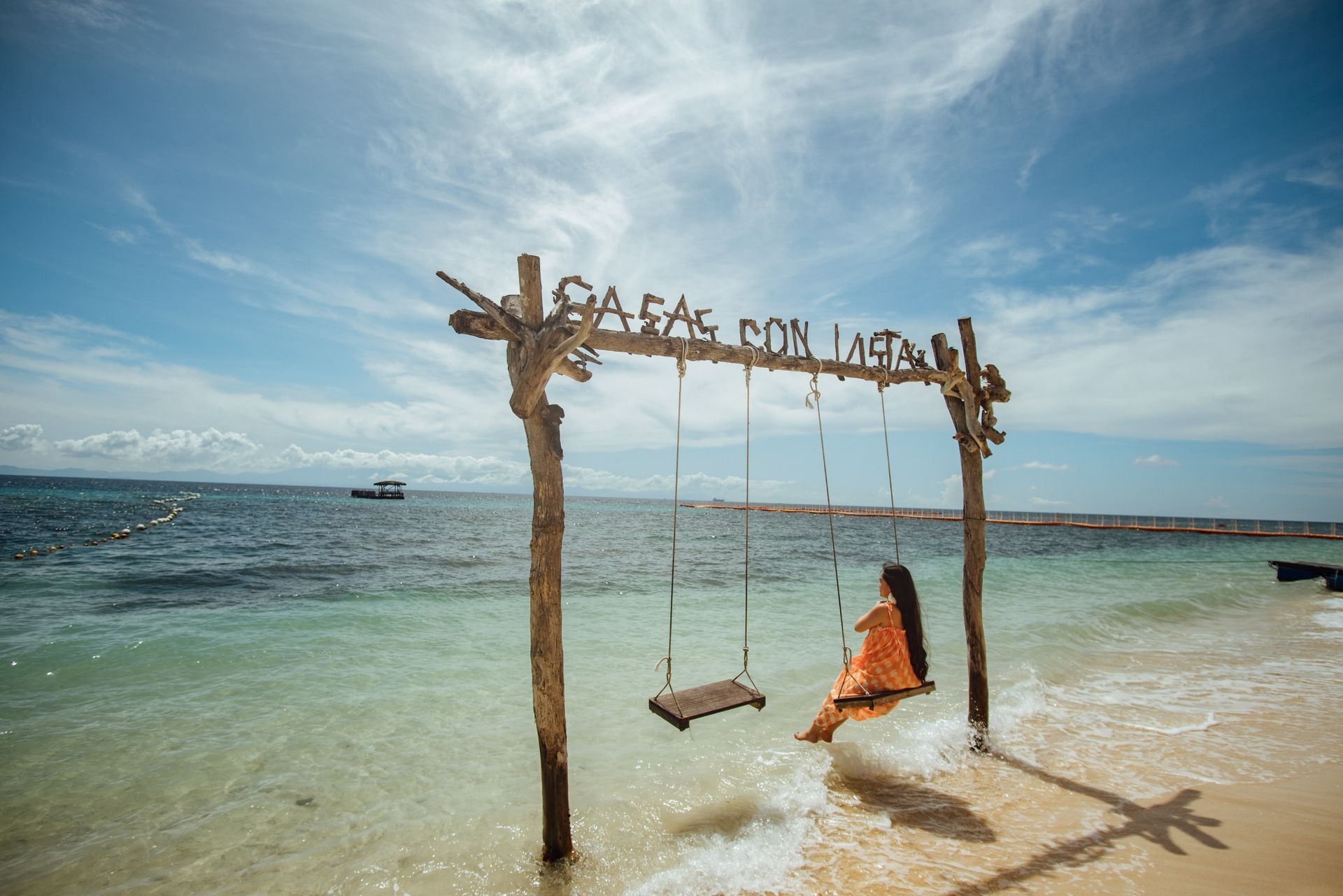 A woman is sitting on a swing in the water on a beach.