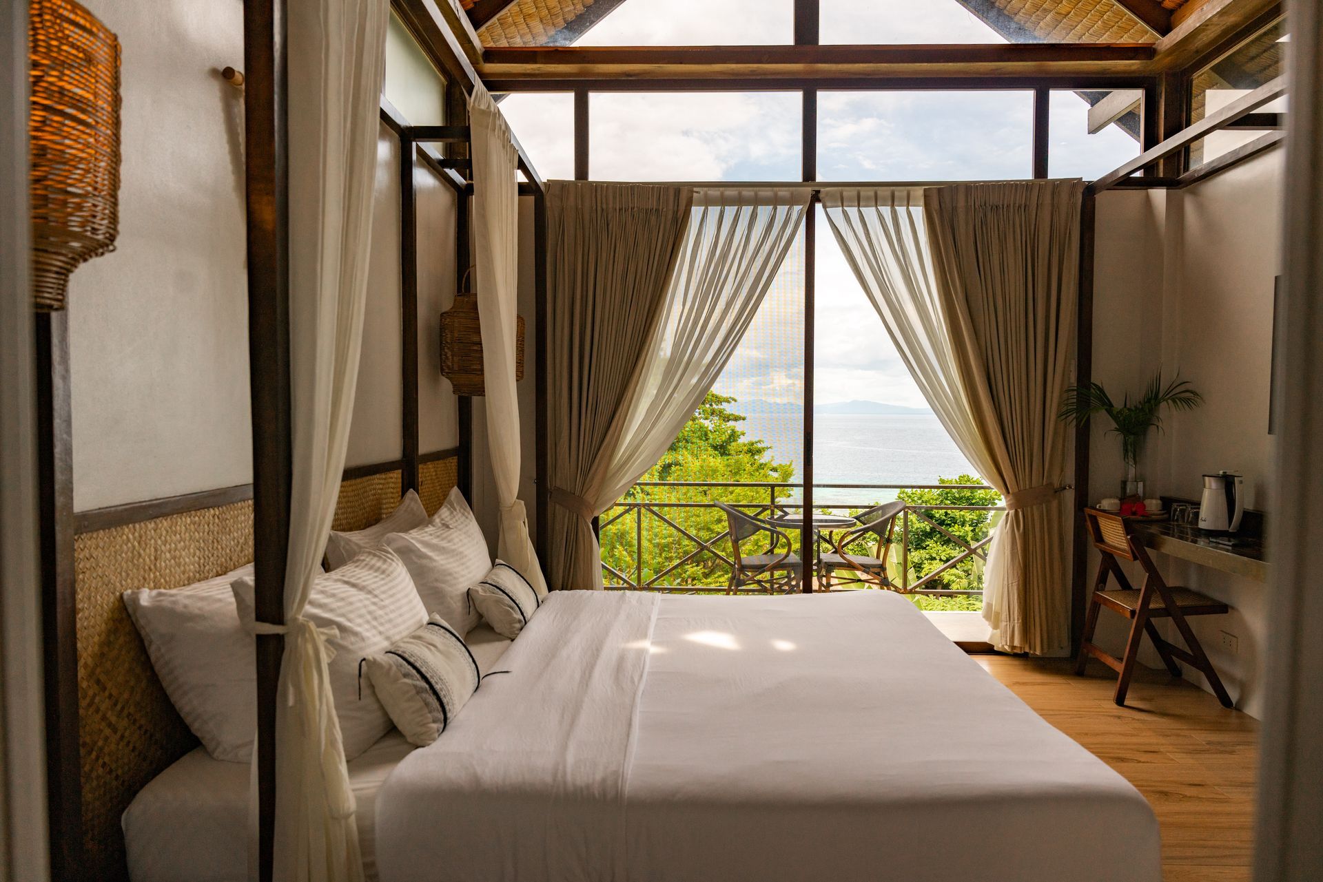A bedroom with a canopy bed and a balcony with a view of the ocean.