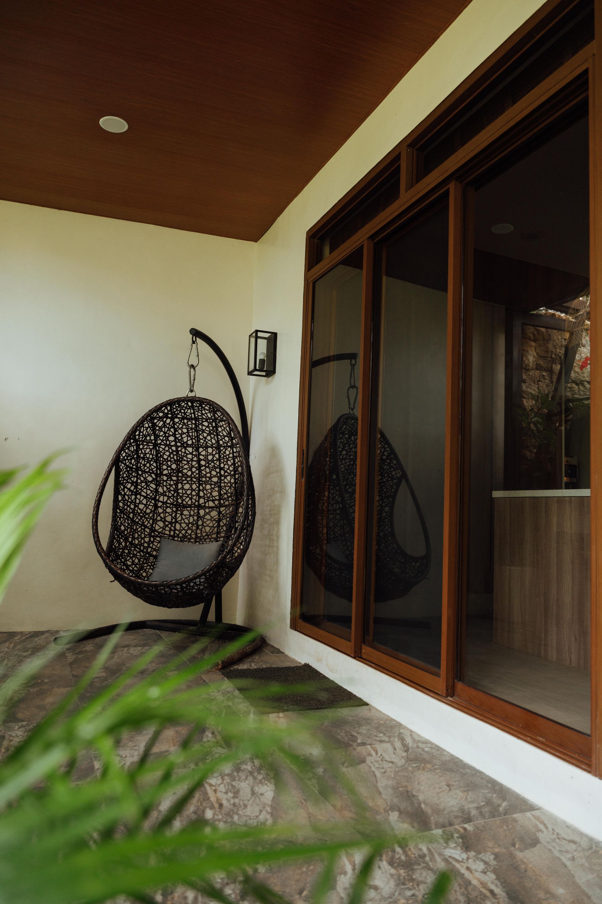 A hanging chair is sitting on a balcony next to a window.