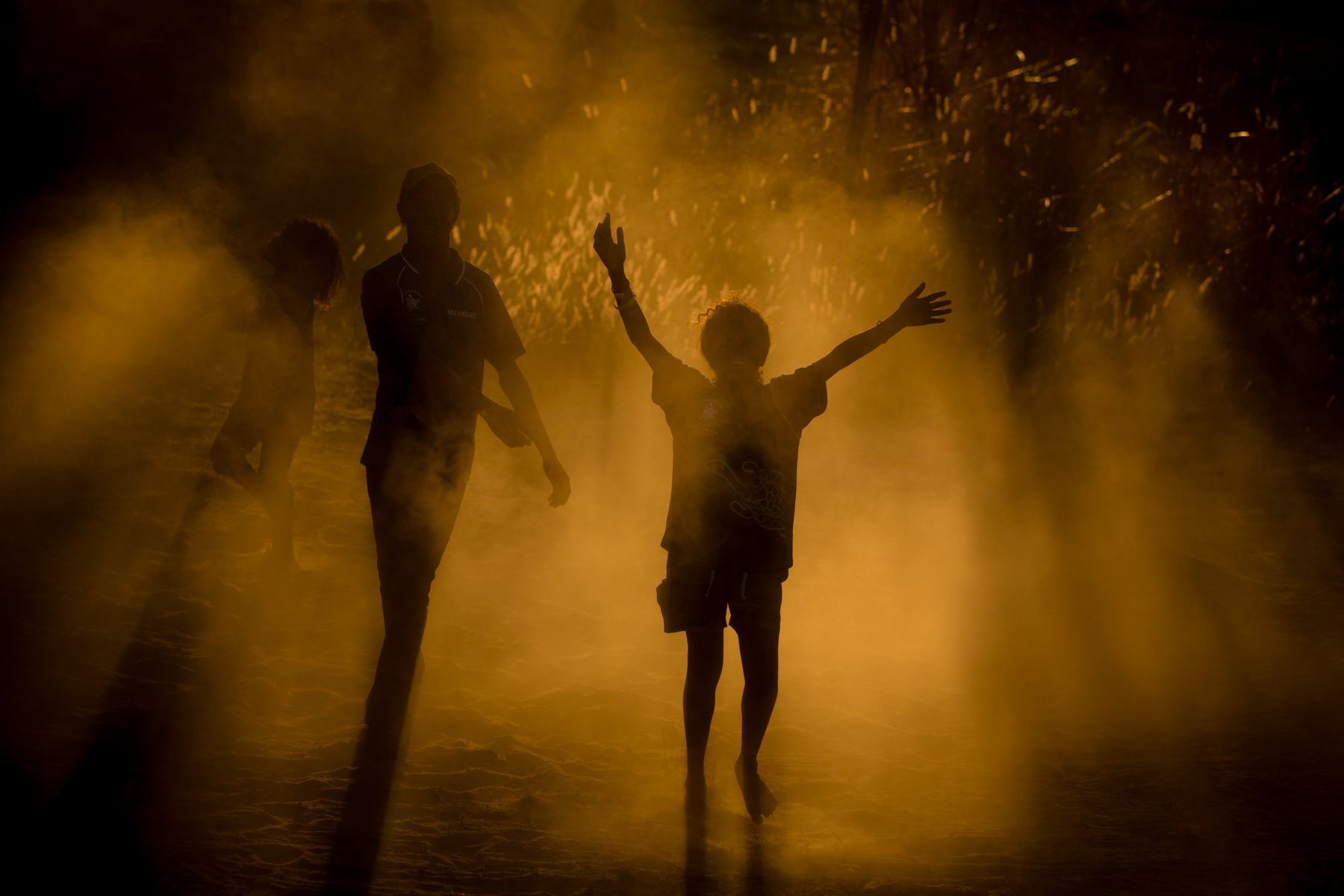 A man and a boy are standing in a foggy forest with their arms outstretched.