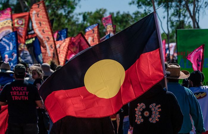 A man is holding an aboriginal flag in front of a crowd of people.