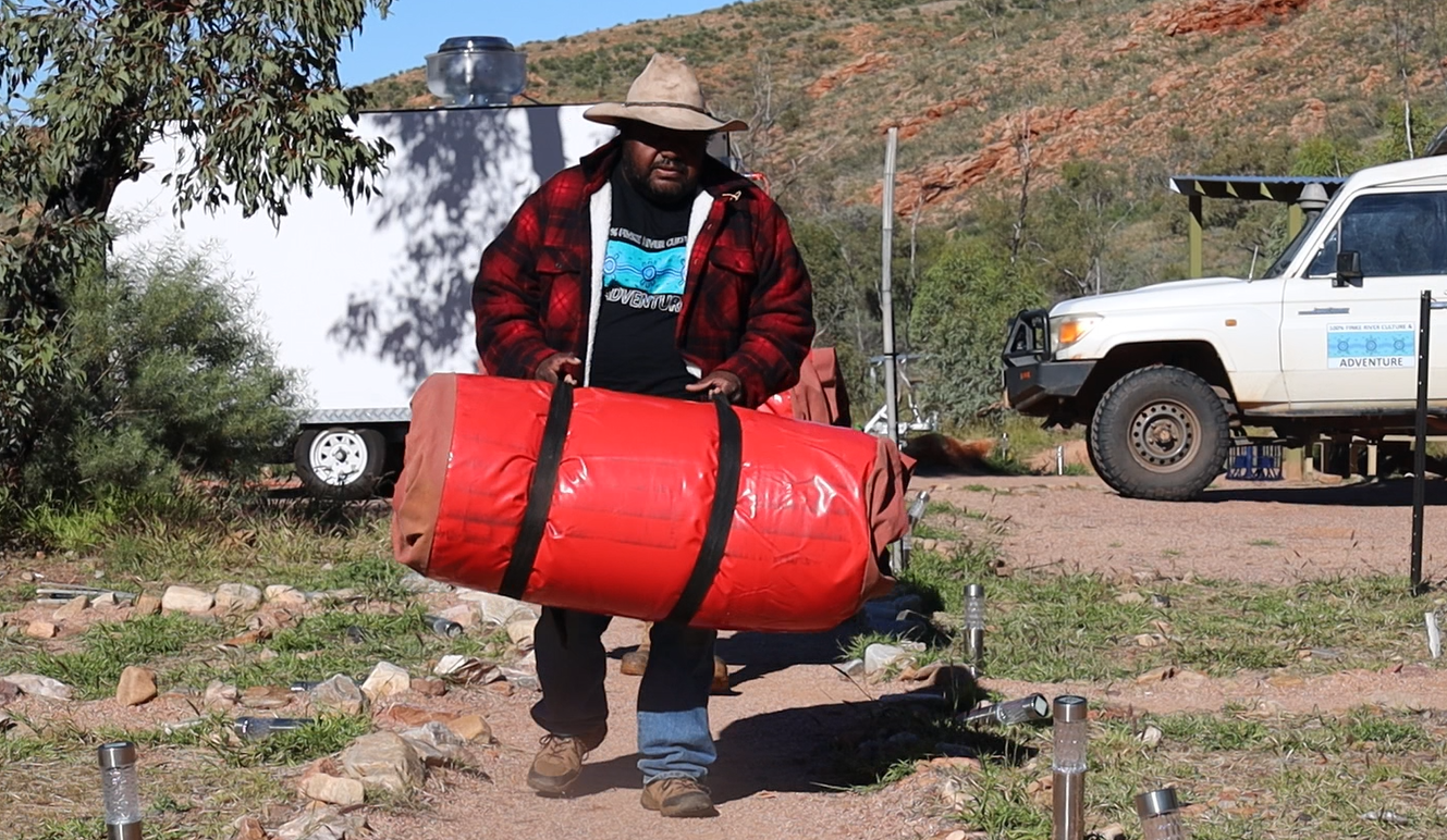 A man is carrying a large red barrel in a field.