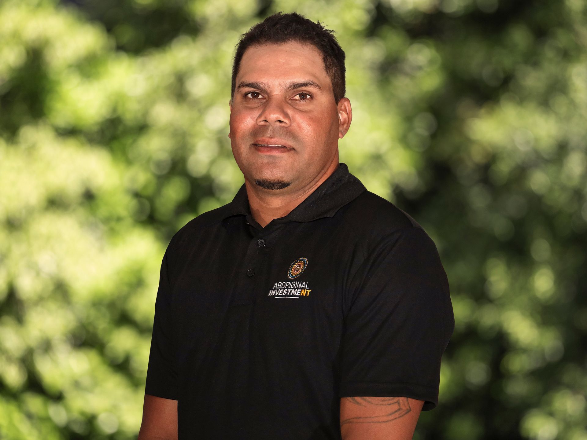 A man wearing a blue polo shirt is standing in front of a white wall.