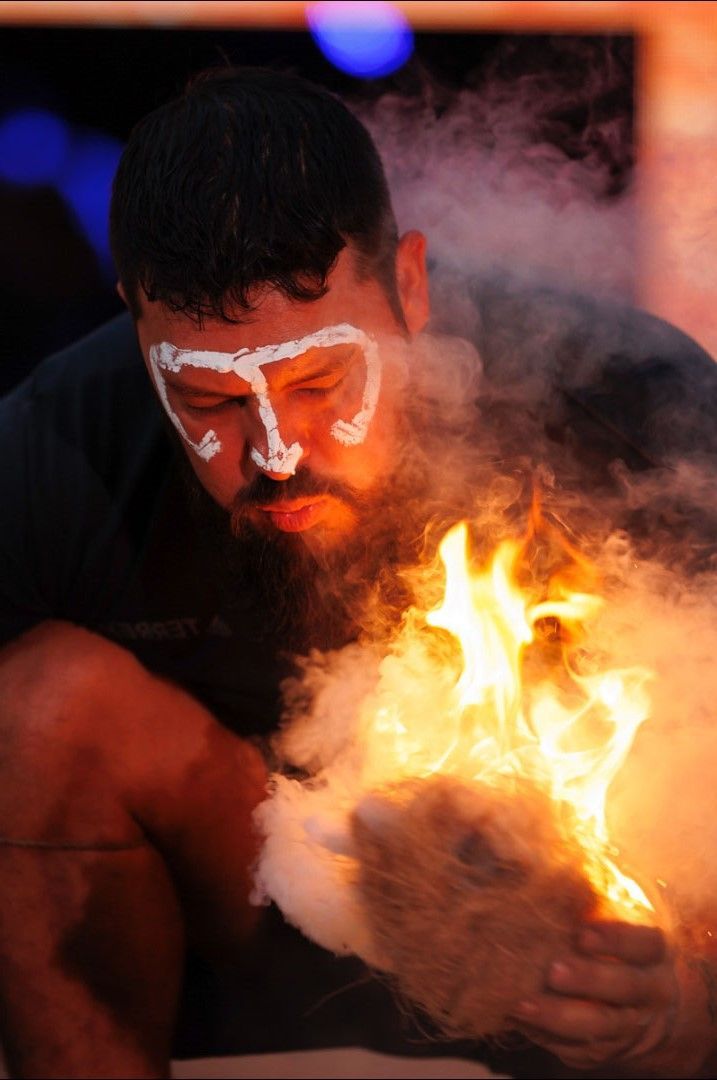 A man with white paint on his face is holding a fire