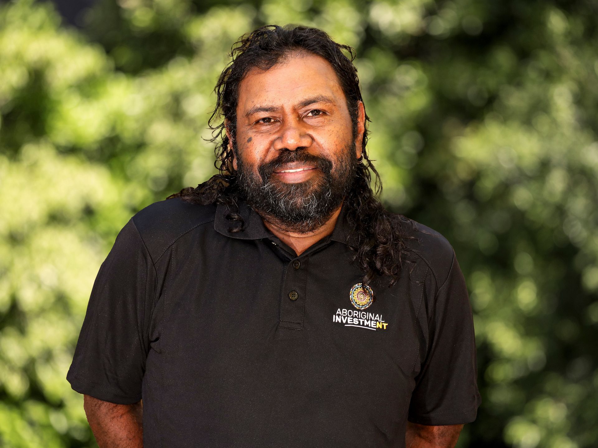 A man with long hair and a beard is wearing a black shirt.