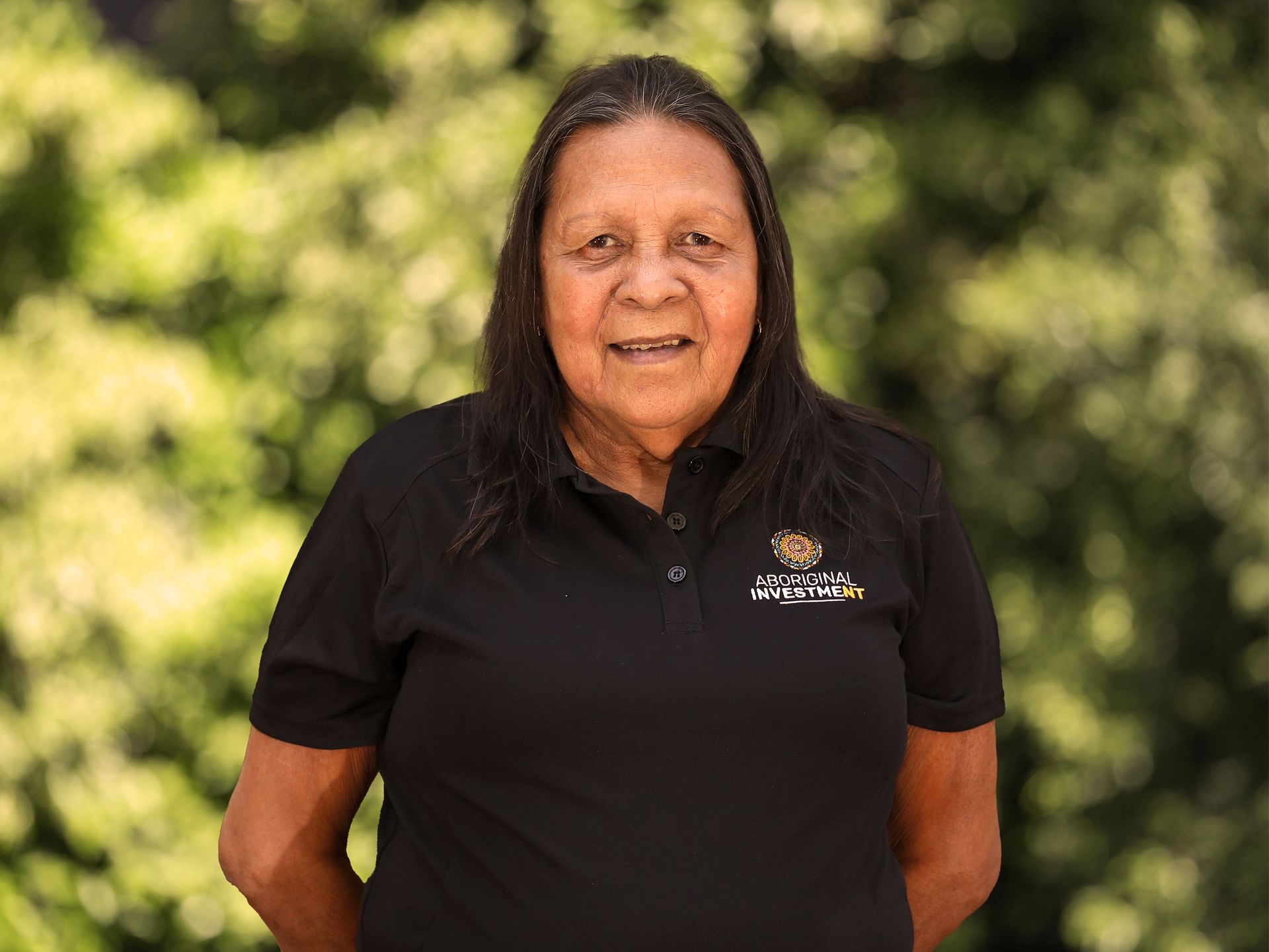 A woman in a black shirt is standing in front of trees.