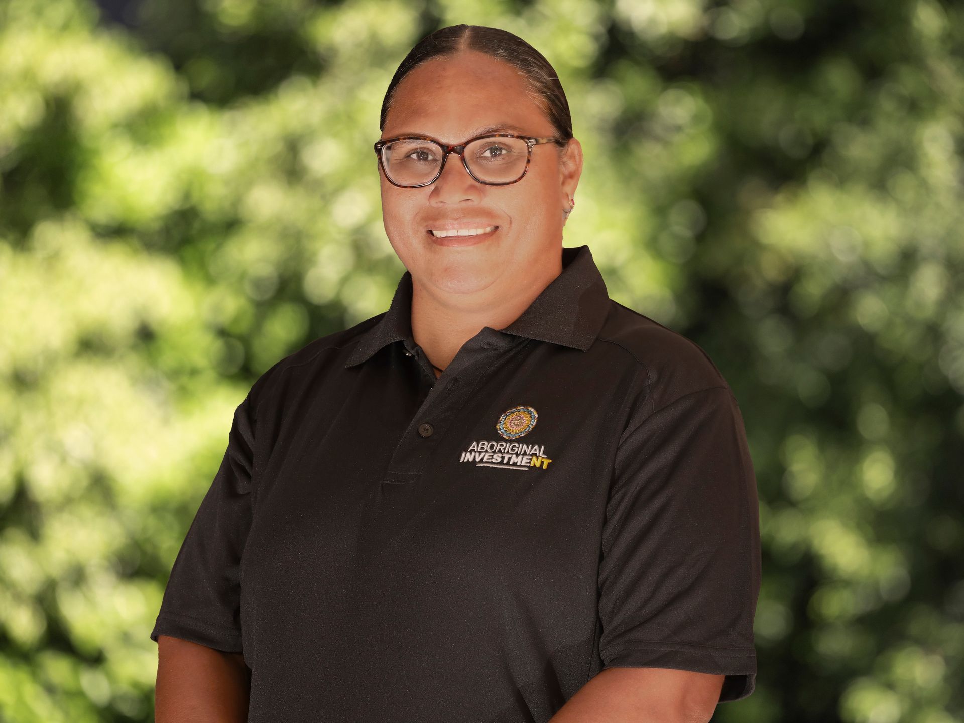 A woman wearing glasses and a black polo shirt is smiling for the camera.