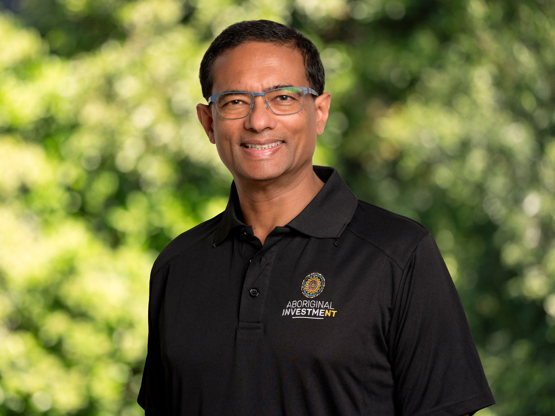 A man wearing glasses and a black polo shirt is smiling for the camera.