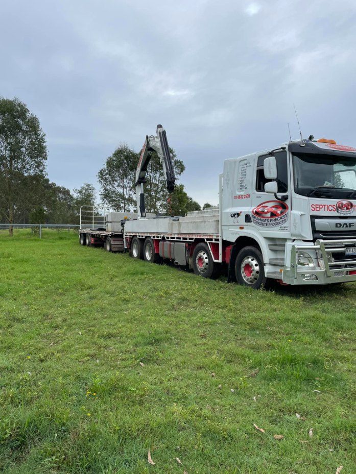 A Truck With a Crane on the Back is Parked in a Grassy Field — Graham's Precast Concrete Products Pty Ltd in Kyogle, NSW
