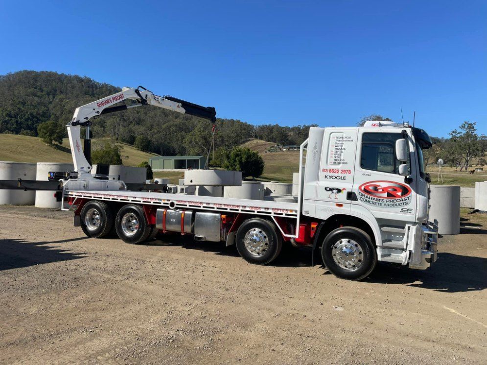 A White Truck With a Crane on the Back is Parked in a Dirt Lot — Graham's Precast Concrete Products Pty Ltd in Kyogle, NSW
