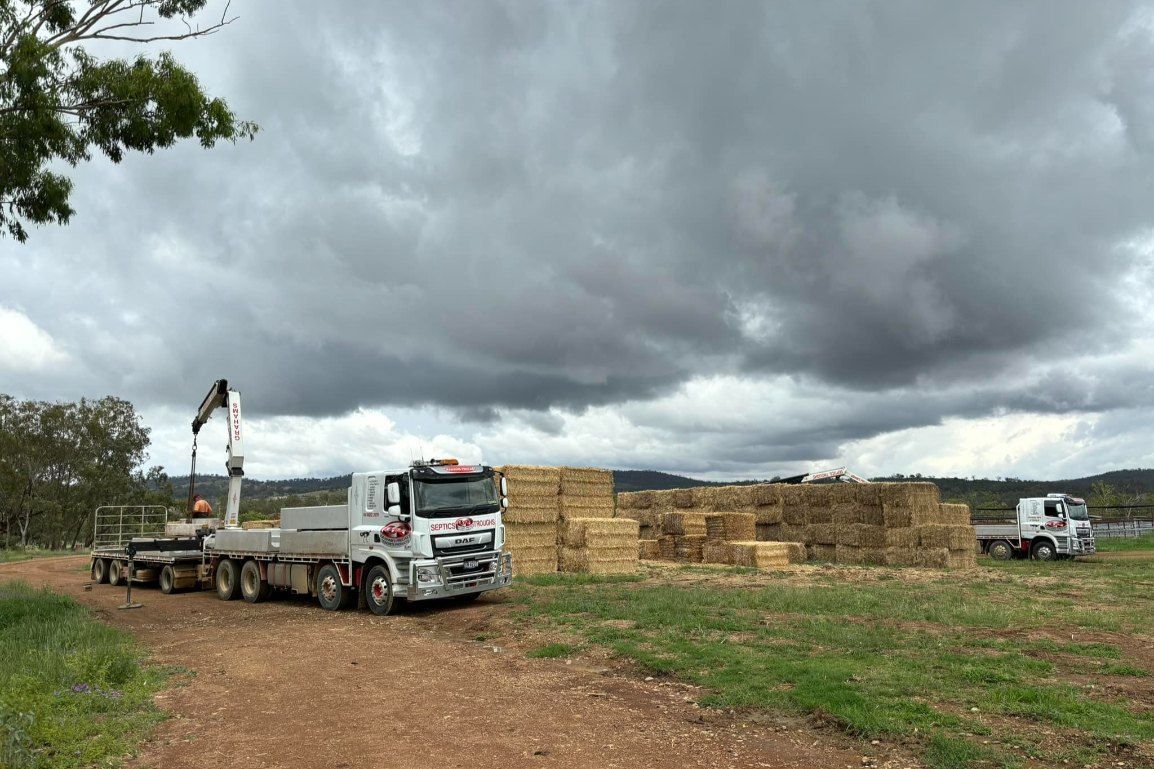 A Truck is Driving Down a Dirt Road Next to a Pile of Hay — Graham's Precast Concrete Products Pty Ltd in Kyogle, NSW