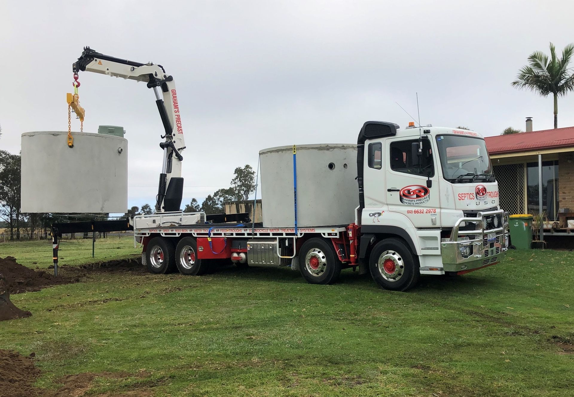 Truck with a crane lifting a large concrete tank in a grassy yard near a house— Graham's Precast Concrete Products Pty Ltd in Kyogle, NSW