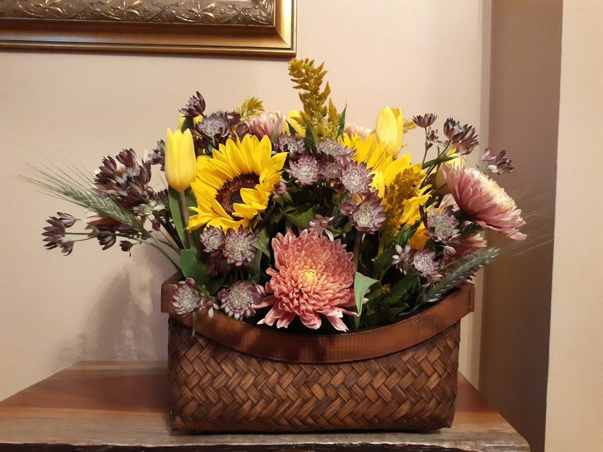 A basket filled with flowers including sunflowers and chrysanthemums
