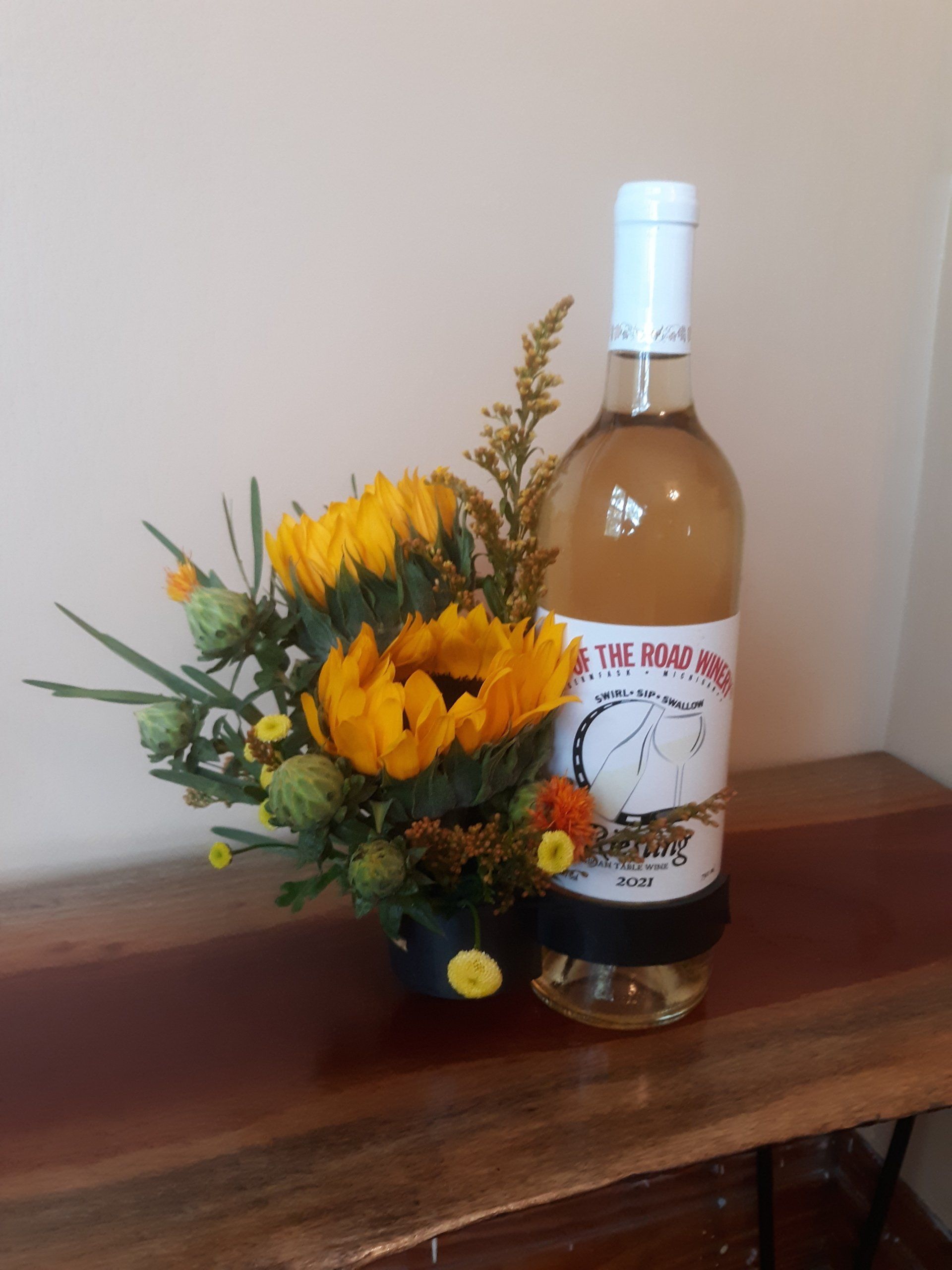 A bottle of wine next to a vase of yellow flowers