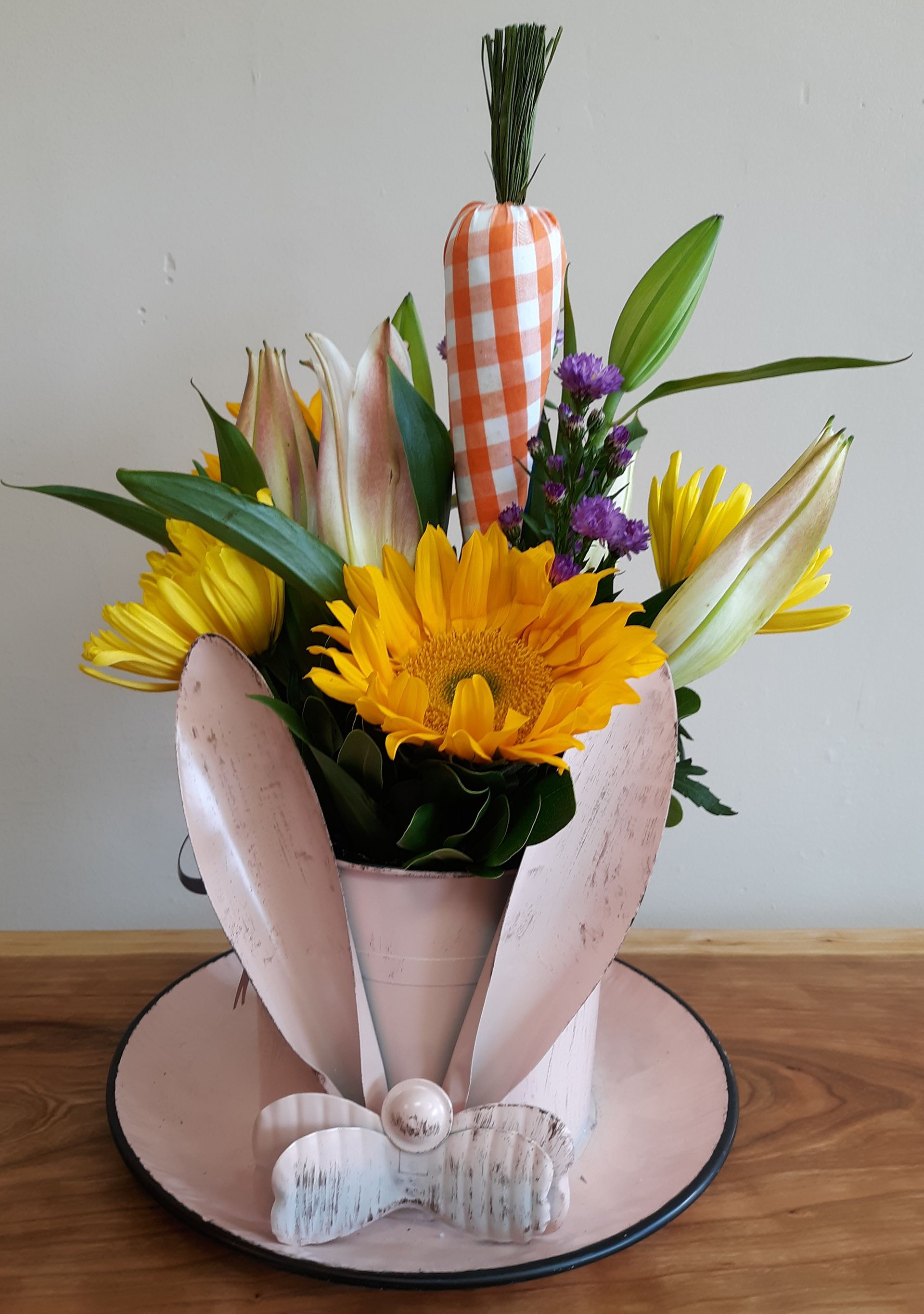 A bouquet of flowers in a teacup with bunny ears and a carrot on top.