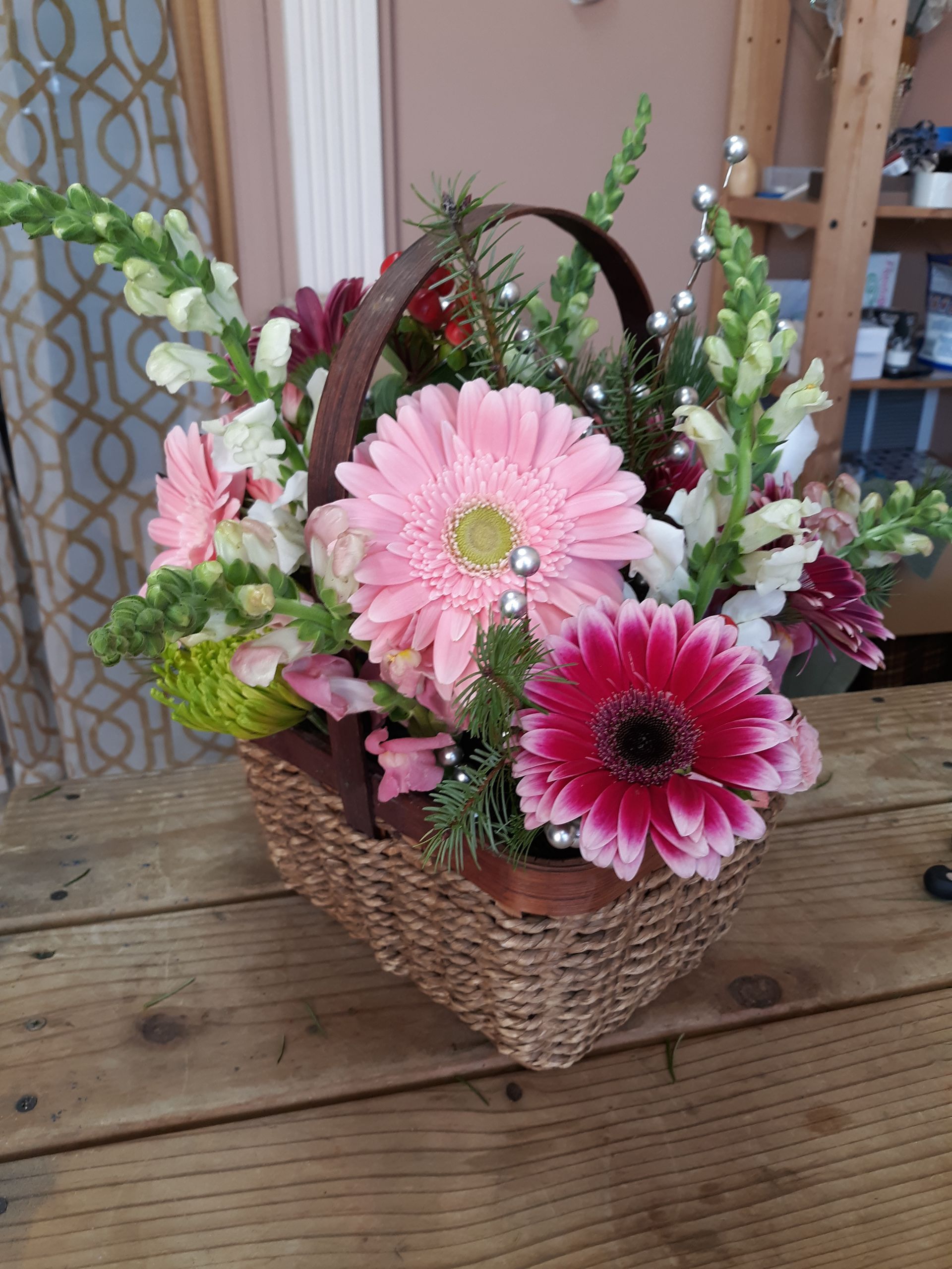 A basket filled with pink and white flowers is sitting on a wooden table.