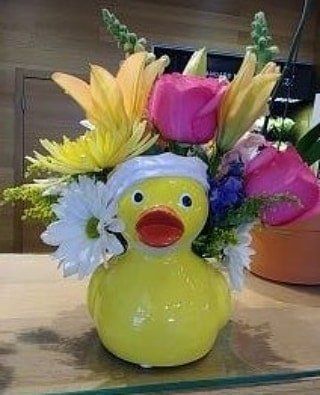 A yellow rubber duck filled with flowers on a table.
