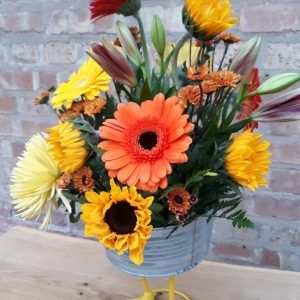 A vase filled with yellow and orange flowers against a brick wall