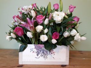 A box filled with pink and white flowers is sitting on a wooden table.