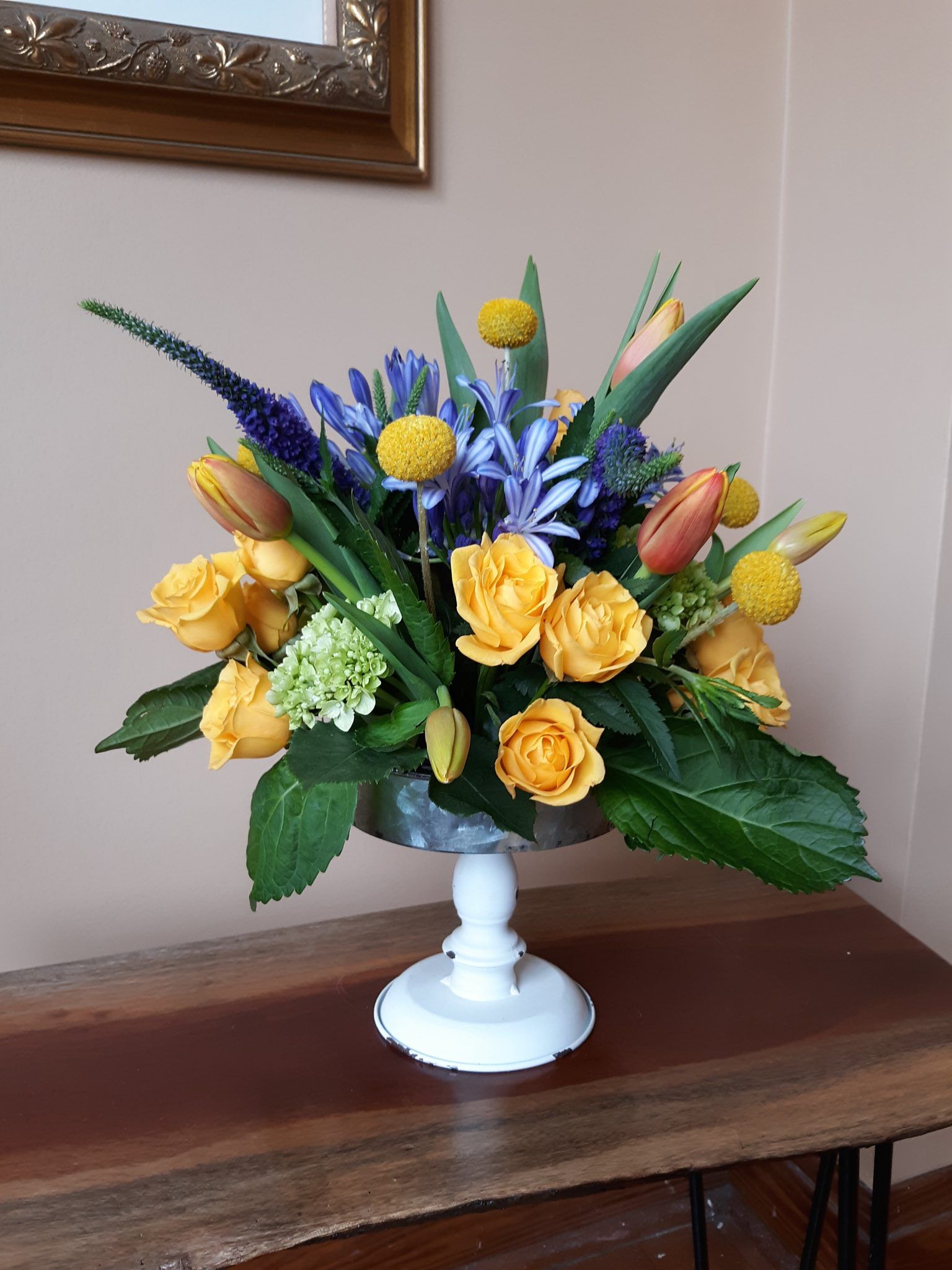 A vase filled with yellow and blue flowers is sitting on a wooden table.