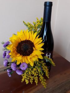 A bottle of wine with a sunflower and purple flowers in it