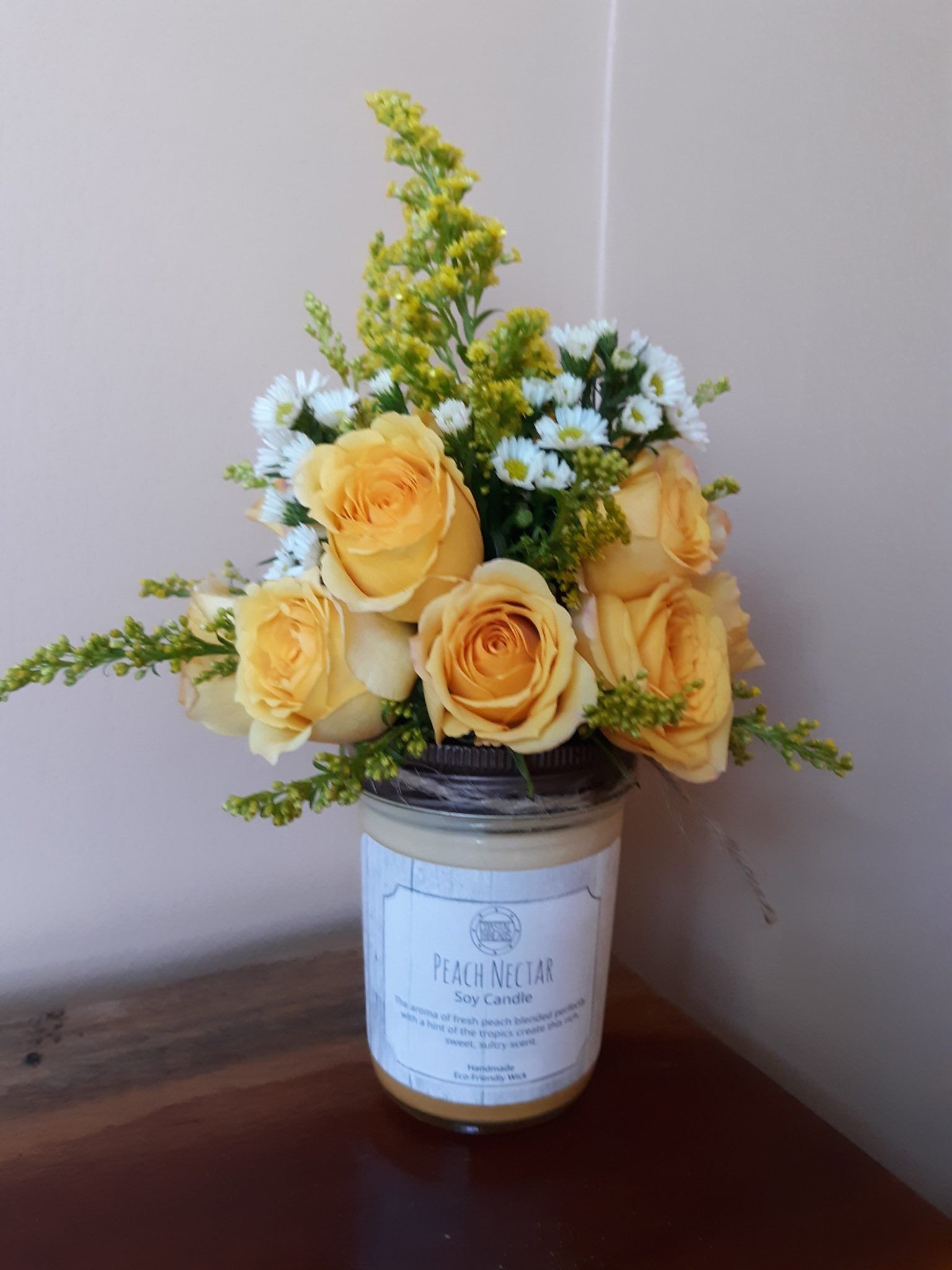 A jar filled with yellow roses and daisies is sitting on a table.