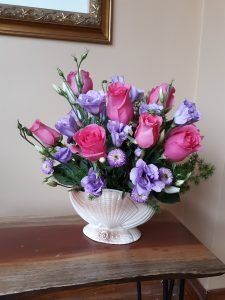 A vase filled with pink and purple flowers is sitting on a wooden table.