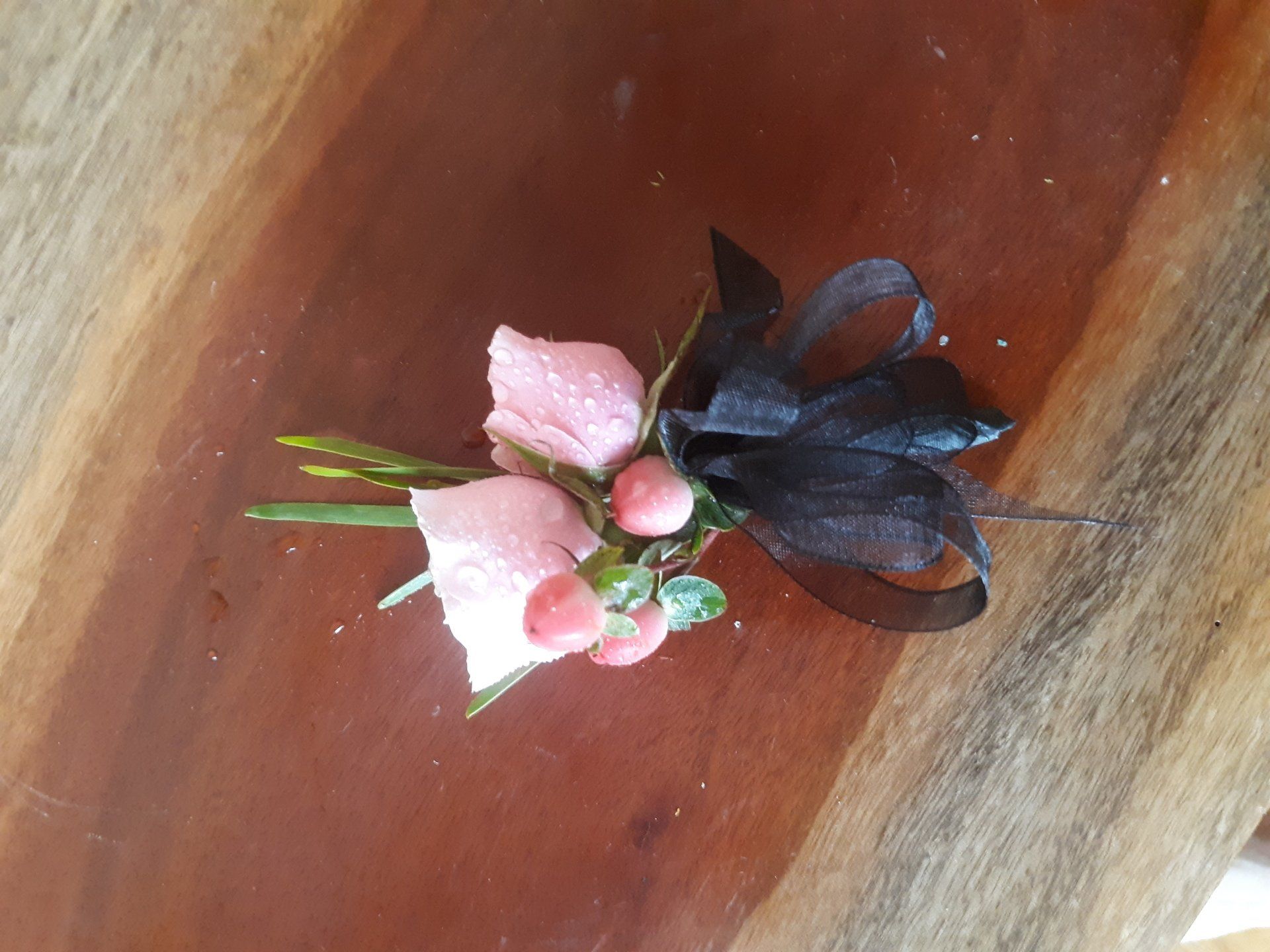 A small bouquet of pink flowers with a black ribbon on a wooden table.