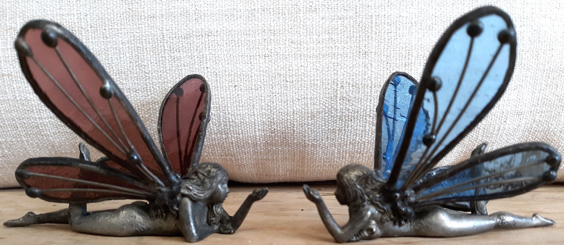 Two figurines of fairies with wings are sitting on a wooden table.