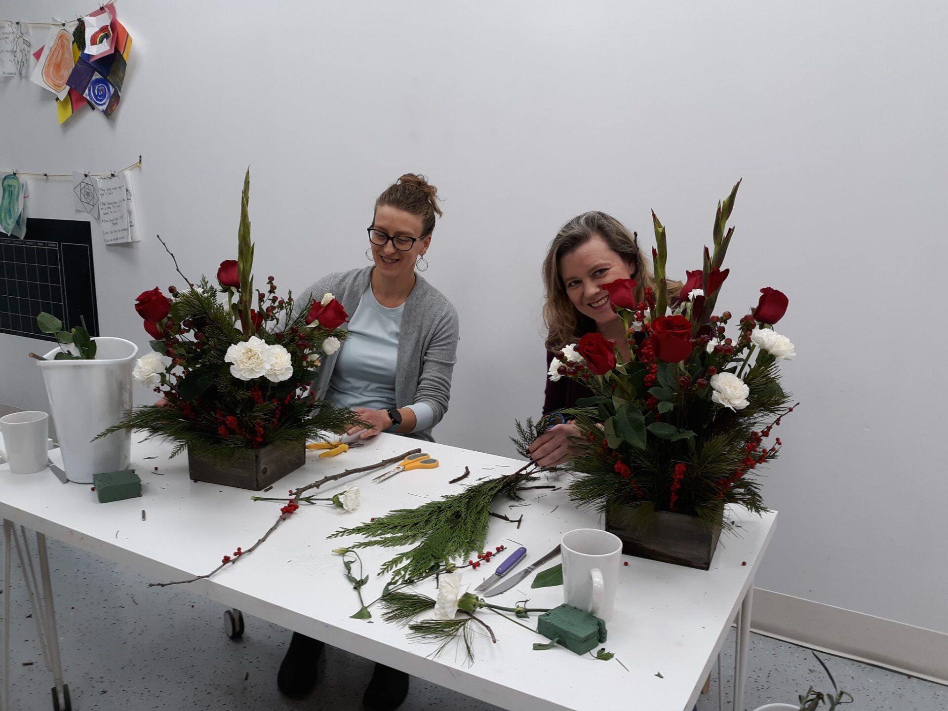 Two women are sitting at a table with flowers in vases.