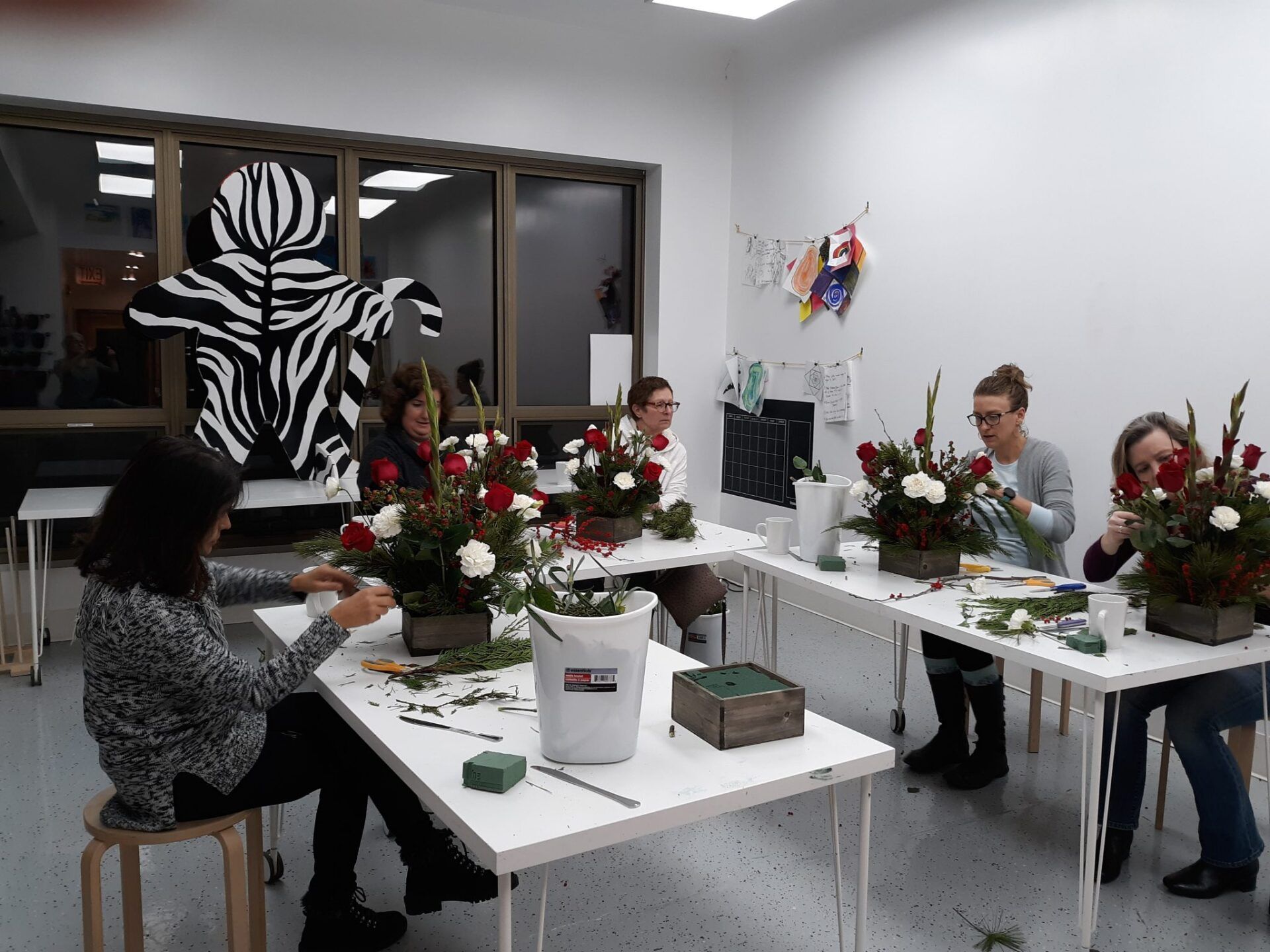 A group of people are sitting at tables in a room making flowers.