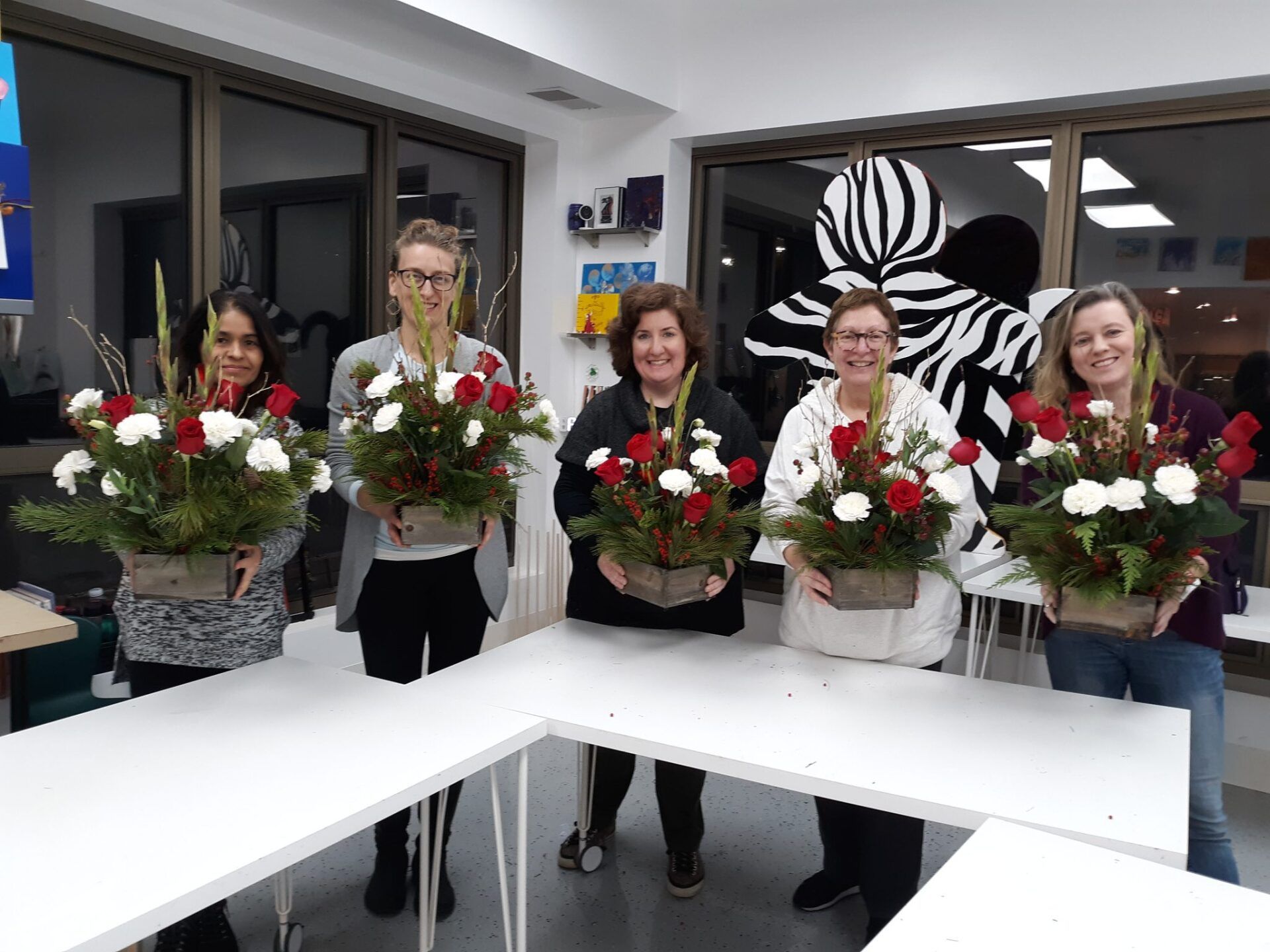 A group of women are standing around a table holding vases of flowers.