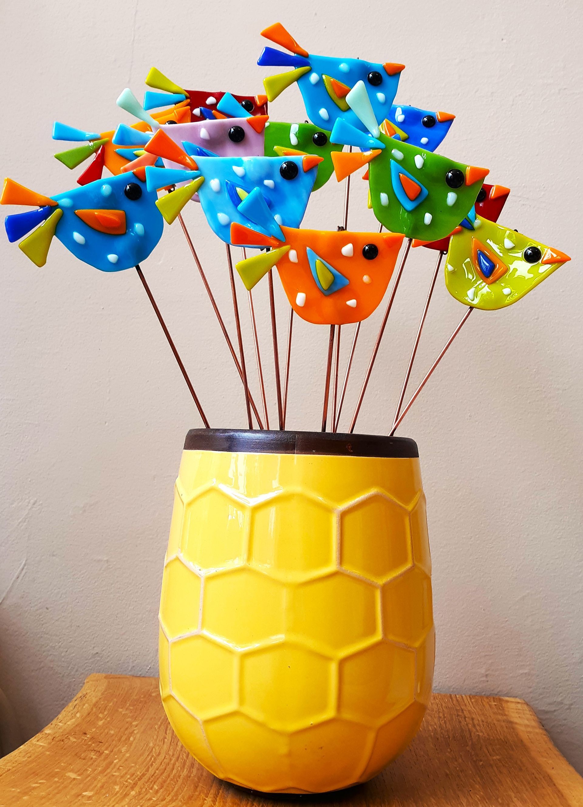 A yellow vase filled with colorful birds on sticks