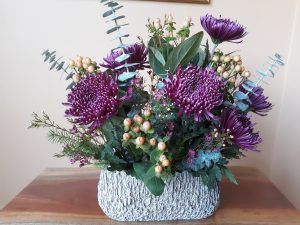 A vase filled with purple flowers is sitting on a wooden table.