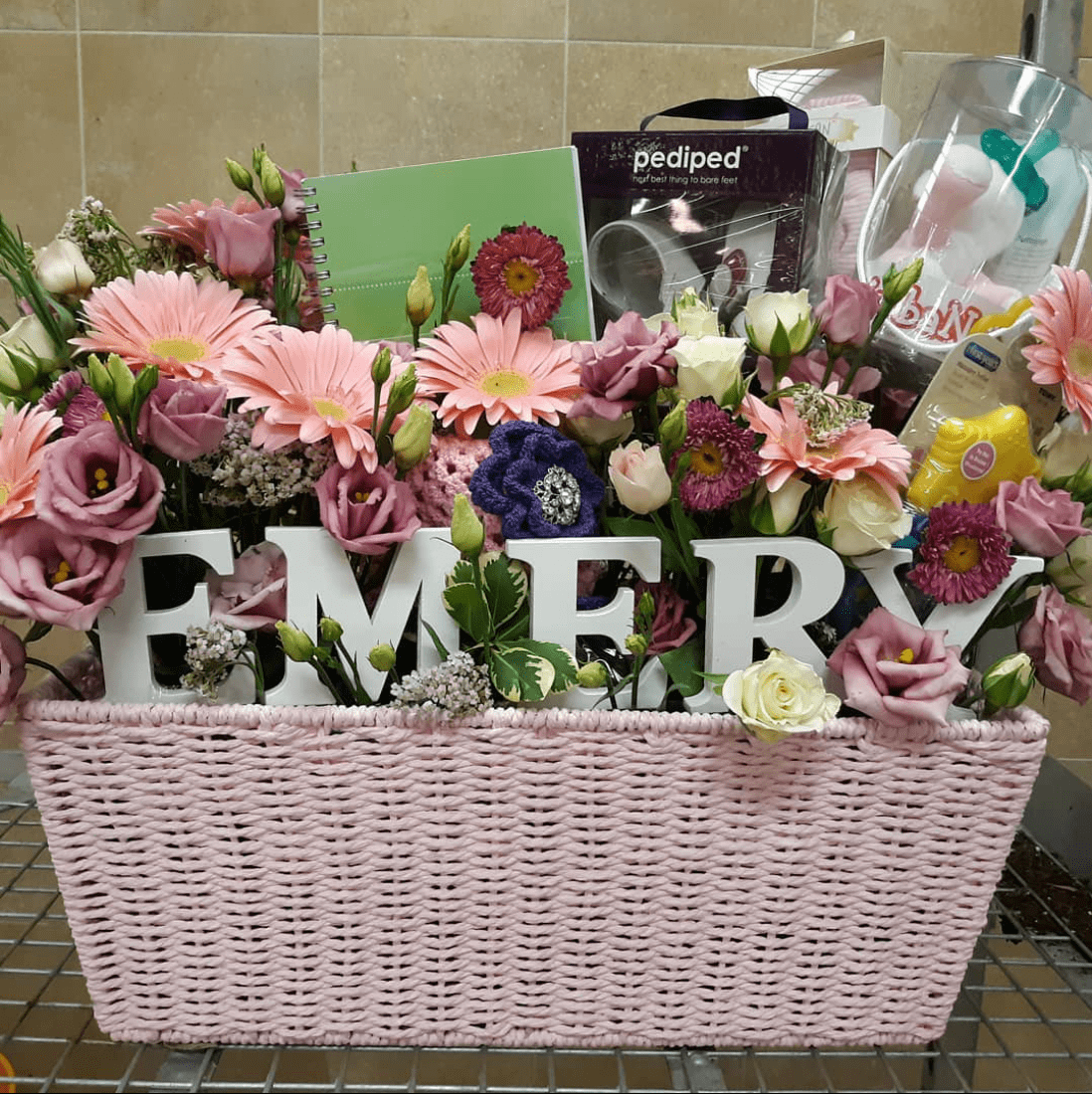 A pink wicker basket filled with flowers and the word emery.