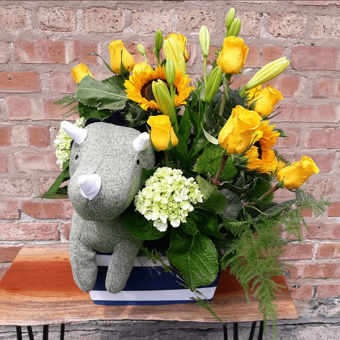 A stuffed rhino is sitting in a vase of flowers.