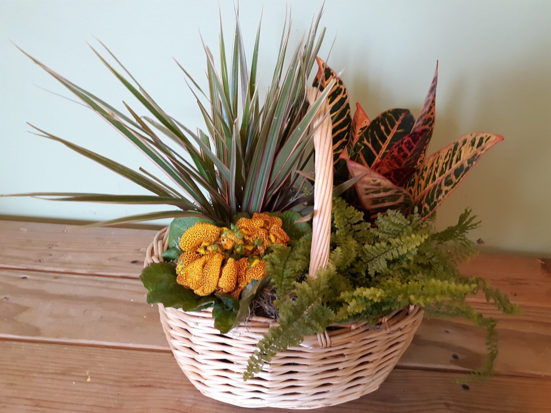 A basket filled with plants and flowers is sitting on a wooden table.