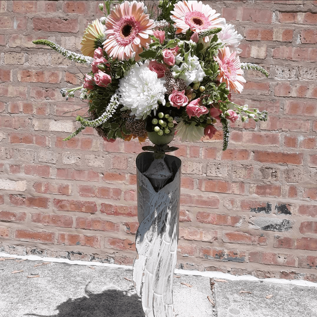 A vase filled with pink and white flowers in front of a brick wall