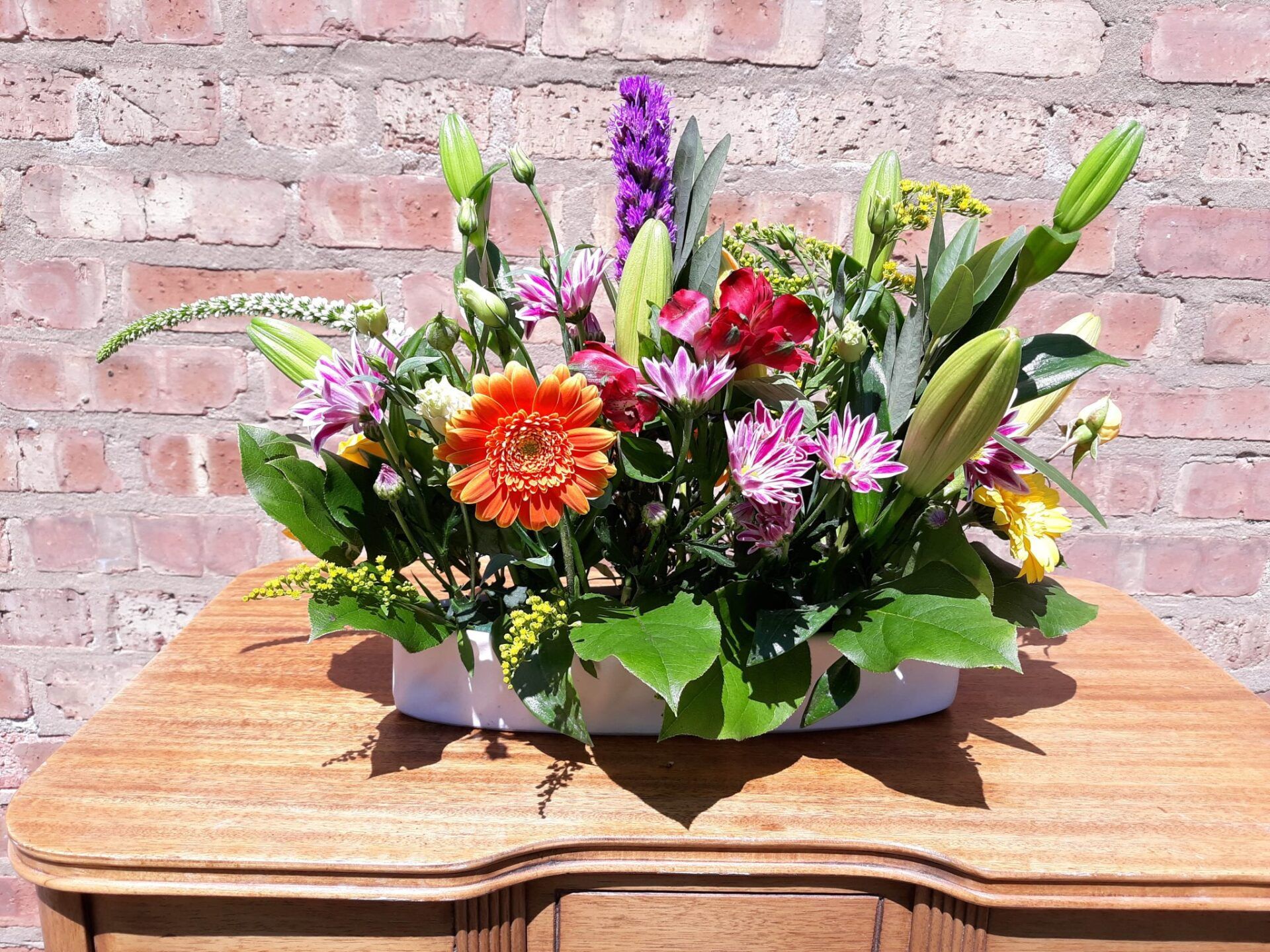 A vase of flowers is sitting on a wooden table in front of a brick wall