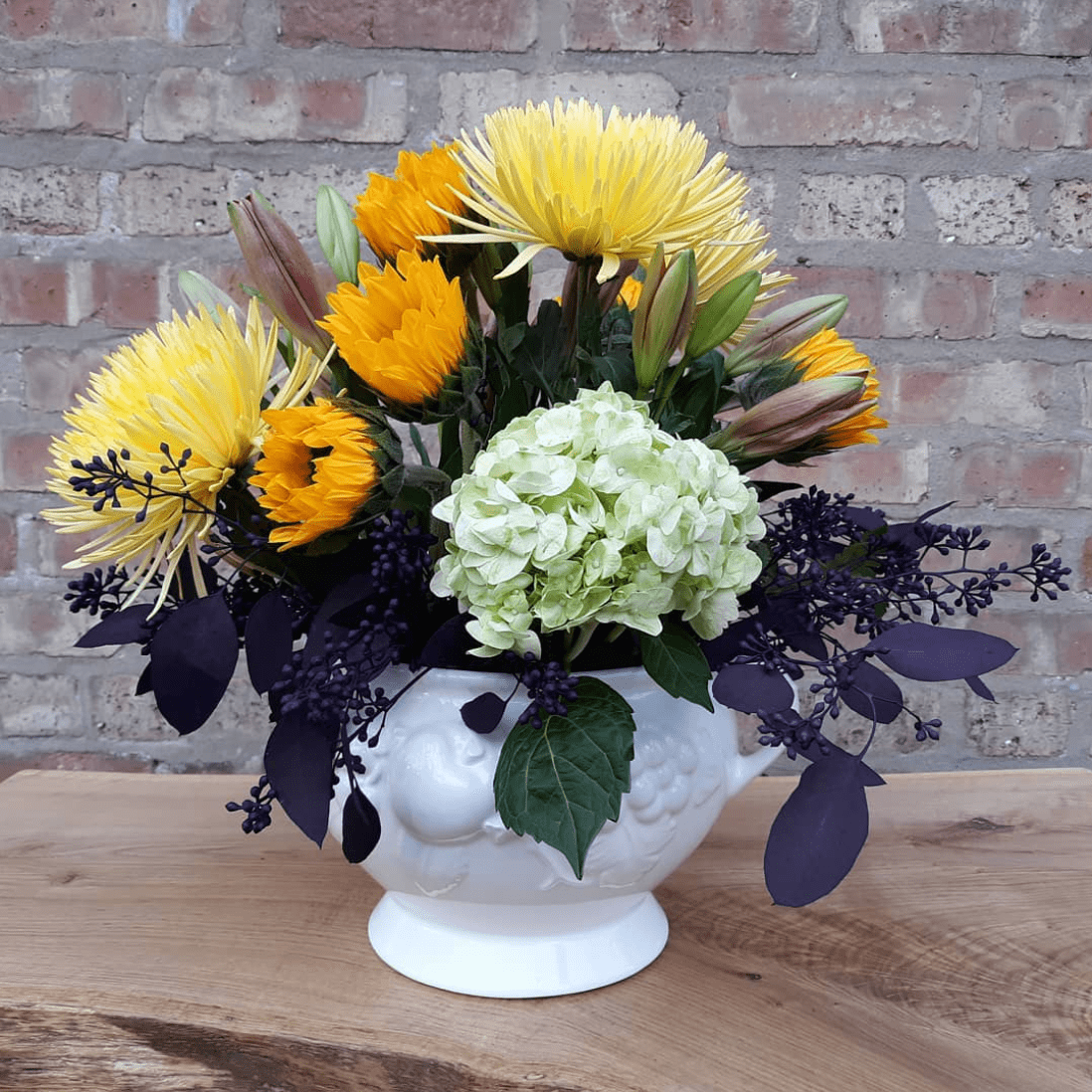 A vase filled with yellow and green flowers is sitting on a wooden table.