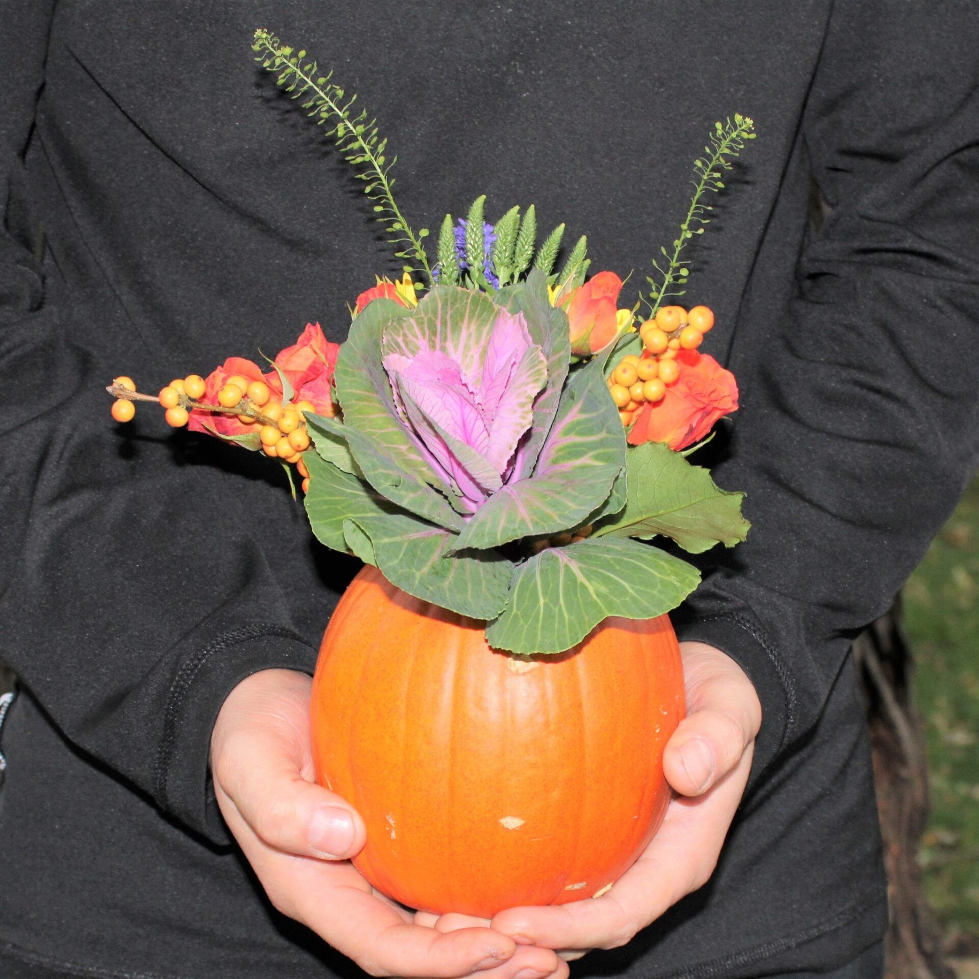 A person is holding a pumpkin with flowers in it