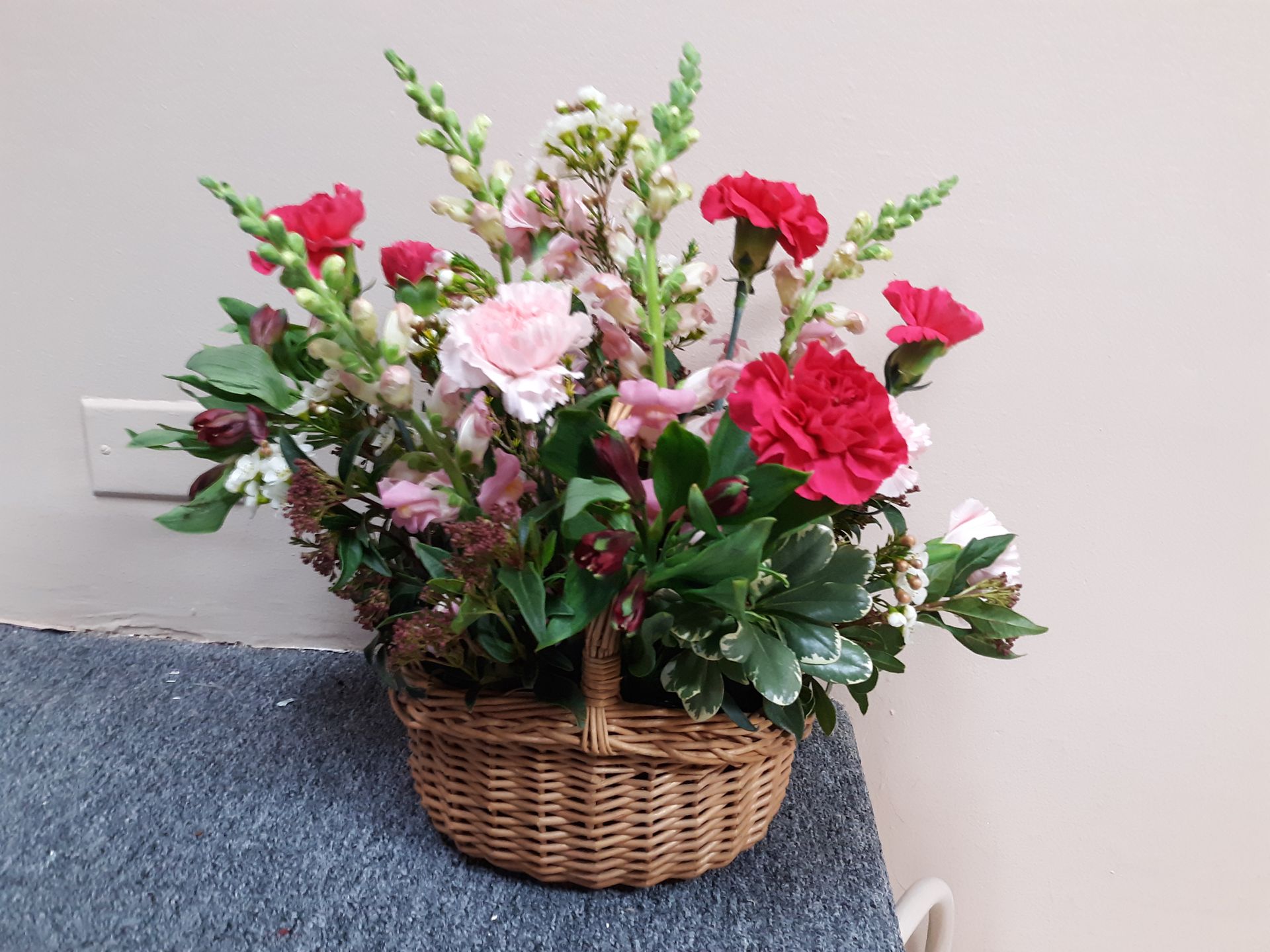 A basket filled with red and pink flowers is sitting on a table.