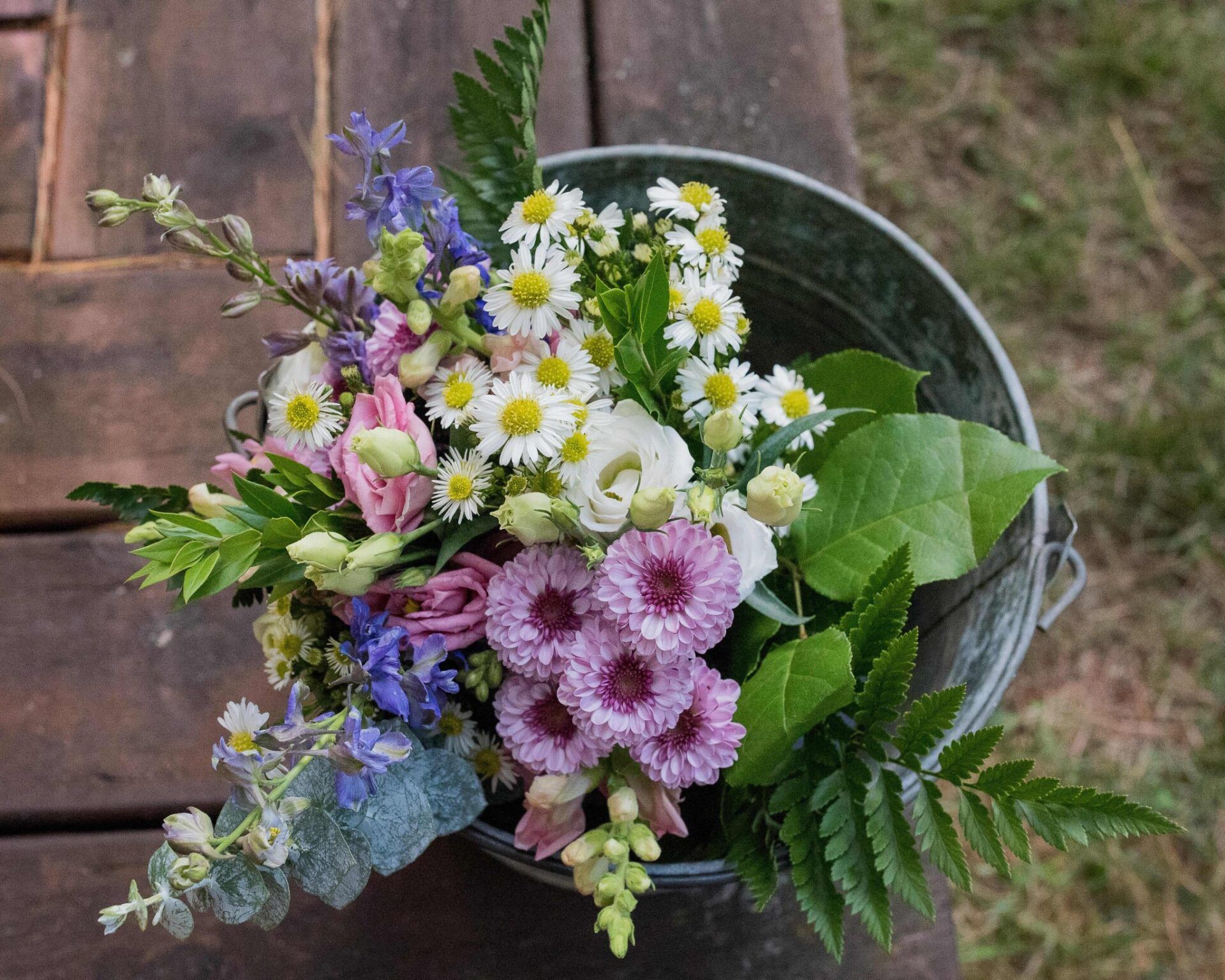 A bucket filled with flowers is sitting on a wooden table.
